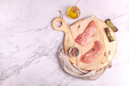 Photo for Raw veal escalope ready to cook on a round cutting board - Royalty Free Image