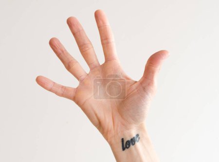 Photo for Women's open hand with fingers outstretched and love tattoo on wrist - Royalty Free Image