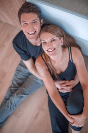 Téléchargez les photos : Heureux jeune couple assis sur le sol et regardant la caméra - en image libre de droit