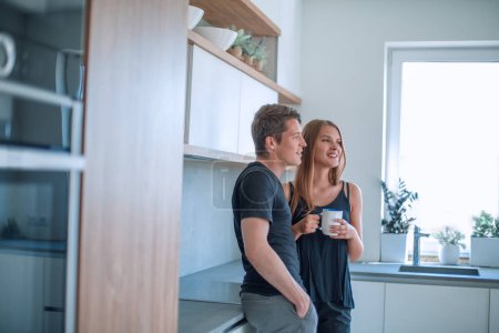 Téléchargez les photos : Heureux jeune couple debout dans la cuisine dans leur maison. - en image libre de droit