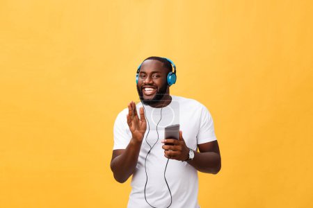 Foto de "Hombre afroamericano con auriculares escuchar y bailar con música. Aislado sobre fondo amarillo
" - Imagen libre de derechos