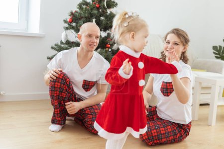 Foto de Toddler child with cochlear implant plays with parents under christmas tree - deafness and innovating medical technologies for hearing aid - Imagen libre de derechos