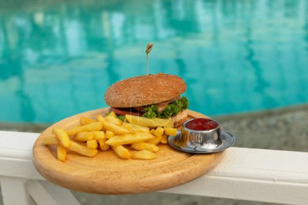 Téléchargez les photos : "hamburger savoureux, frites et ketchup appétissants. concept de détente et de manger au bord de la mer par une journée lumineuse, chaude et ensoleillée sur la plage. foyer doux" - en image libre de droit