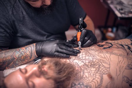 Téléchargez les photos : Tatoueur travaillant sur un appareil professionnel de tatouage dans un studio de tatouage - en image libre de droit