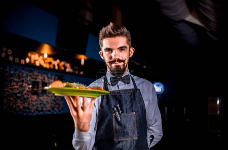 Photo for Professional friendly waiter helpfully serves cooked dish on a black background. - Royalty Free Image
