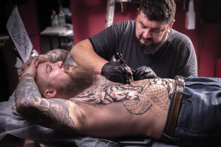 Photo for Tattooist demonstrates the process of getting tattoo in tattoo parlor - Royalty Free Image