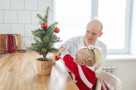 Téléchargez les photos : Child with cochlear implant hearing aid having fun with father and small christmas tree - diversity and deafness treatment and medical innovative technologies - en image libre de droit