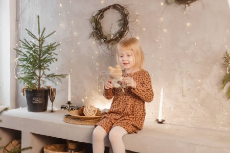 Foto de Una chica está jugando en Nochebuena en una hermosa casa decorada para las vacaciones de Año Nuevo. Interior de estilo escandinavo con abetos vivos y una escalera de madera. - Imagen libre de derechos