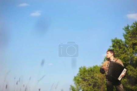 Foto de Un hombre con ropa eslava tradicional tocando un acordeón en medio del bosque - Imagen libre de derechos