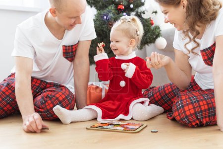 Foto de Toddler child with cochlear implant plays with parents under christmas tree - deafness and innovating medical technologies for hearing aid and diversity - Imagen libre de derechos