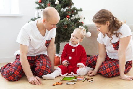 Photo for Toddler child with cochlear implant plays with parents under christmas tree - deafness and innovating medical technologies for hearing aid and diversity - Royalty Free Image