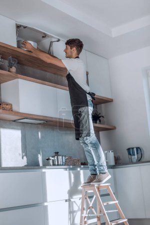 Photo for Man standing on a stepladder in the home kitchen - Royalty Free Image