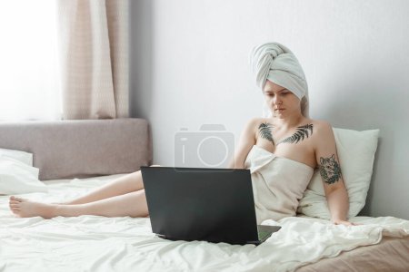 Photo for Tver, Russia-august 2, 2021. A tattooed woman after a shower is lying on the couch with a laptop. - Royalty Free Image