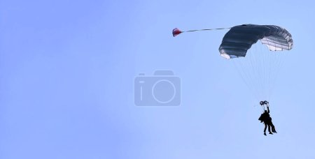 Photo for "A skydiver with a white parachute canopy against a blue sky and white clouds, close-up." - Royalty Free Image