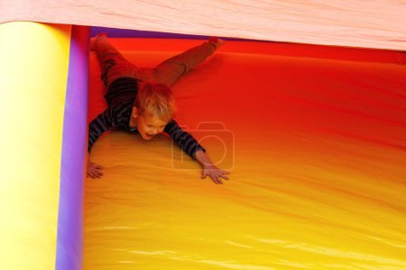 Téléchargez les photos : "A brave little boy slides down on a red-yellow trampoline at an amusement park." - en image libre de droit