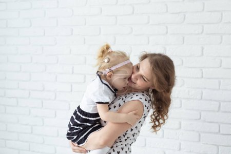 Photo for Mother holds her child with hearing aids and cochlear implants on white brick wall with copy space and place for advertising . Deaf and health concept - Royalty Free Image