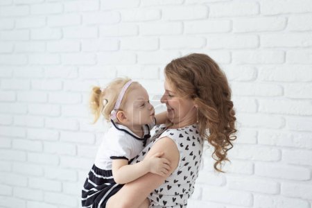 Photo for Mother holds her child with hearing aids and cochlear implants on white brick wall with copy space and place for advertising . Deaf and health concept - Royalty Free Image