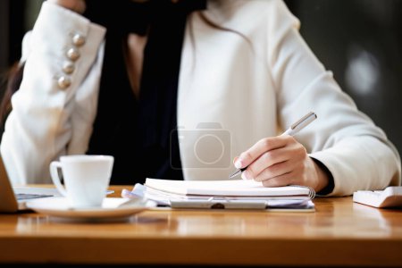 Photo pour "Asiatique femme d'affaires prenant des notes d'affaires tout en parlant au téléphone" - image libre de droit