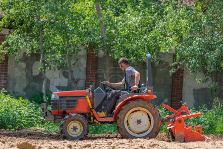 Photo for "A man on a mini-excavator levels a piece of land, loosens the soil." - Royalty Free Image