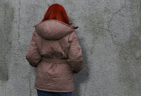 Foto de "Vista trasera de una chica de cabello castaño con una chaqueta marrón contra una pared." - Imagen libre de derechos
