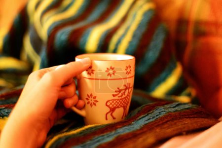 Photo for "Chilling at home under the blanket with remote control and tea mug in hand" - Royalty Free Image