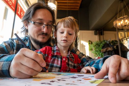 Téléchargez les photos : Portrait d'enfant avec son père dessinant au crayon dans un café - en image libre de droit
