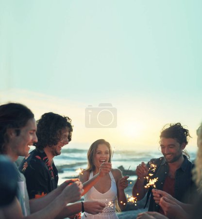 Foto de Friends with sparklers celebrating new years eve on beach at sunset - Imagen libre de derechos