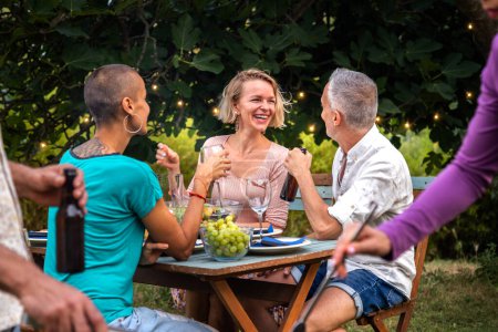 Photo for Adult friends laugh and talk outdoors during garden dinner party. - Royalty Free Image