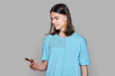 Photo for "Teenager guy with smartphone in his hands on gray colored background" - Royalty Free Image