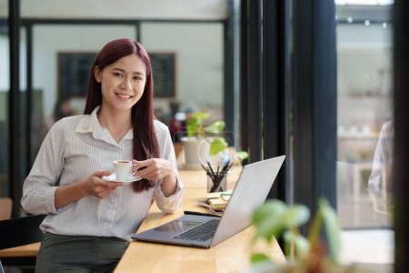 Photo pour "Asiatique femme d'affaires boire du café et en utilisant l'ordinateur dans le bureau" - image libre de droit