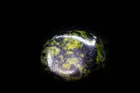 Foto de Primer plano enfocado verde y negro tumbado, liso y brillante piedra de cristal serpentina macro aislado en una superficie de fondo negro - Imagen libre de derechos