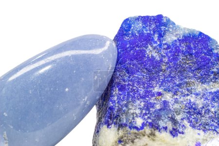 Foto de Macro light blue angelite crystal, shiny tumbled blue anhydrite stone and a deep royal blue lapis lazuli mineral with gold pyrite specks and white calcite veins isolated on a white surface background. Two blue crystals, angelite and lapis lazuli. - Imagen libre de derechos