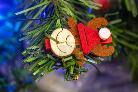Foto de Cute reindeer Christmas ornament stirrup on green fake Christmas tree with blue lights behind. - Imagen libre de derechos