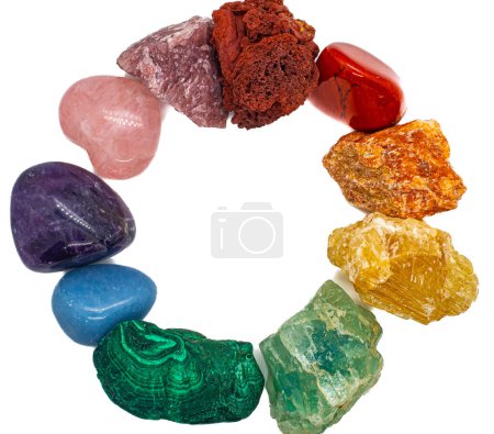 Cristales coloridos arco iris dispuestos en un círculo aislado sobre fondo de superficie blanca. Piedra de lava roja y jaspe, calcita naranja y amarilla, fluorita verde y malaquita, angelita azul, amatista púrpura