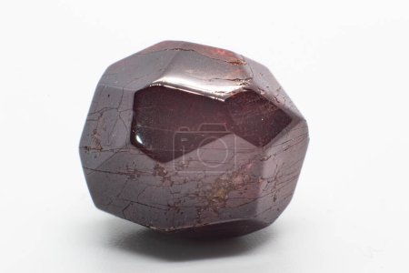 Dodekaedrisches natürliches tiefrotes Granat, leicht getrommelt, polierter Kristall isoliert auf einer weißen Oberfläche, Hintergrund Makrofotografie