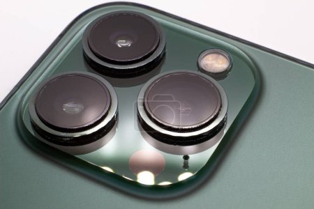 Téléchargez les photos : Close-up focused Alpine Green iPhone 13 Pro with 3 big circular cameras, deep green phone backside and cameras isolated on a white surface background with room for diagonal copy space - en image libre de droit