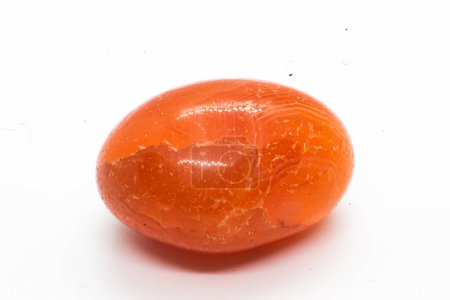 Ehwaz Rune eingraviert in einen undurchsichtigen orangefarbenen Karneol-Quarz aus geschliffenem und poliertem Kristall. Ein orange polierter Mineralkiesel isoliert auf weißem Hintergrund  