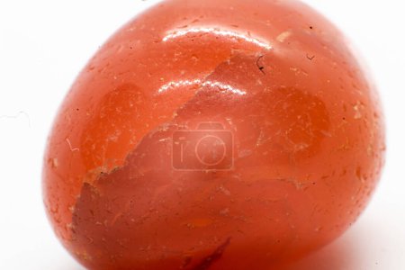 Ehwaz Rune eingraviert in einen undurchsichtigen orangefarbenen Karneol-Quarz aus geschliffenem und poliertem Kristall. Ein orange polierter Mineralkiesel isoliert auf weißem Hintergrund  