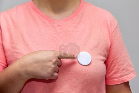 Woman in pink shirt pointing at a shiny round button. Isolated pin badge mockup