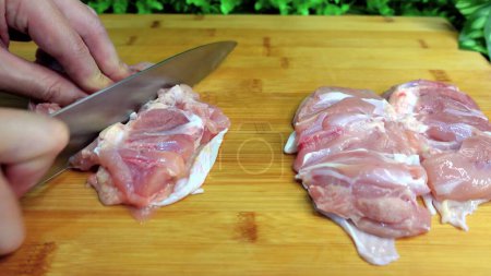 Foto de The cook cuts raw chicken into pieces on a cutting board. - Imagen libre de derechos