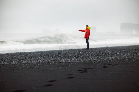 Photo for The man in waterproof jacket and pants standing on the beach with black volcanic sand, Reynisfjara, south of Iceland. Icelandic nature, Atlantic Ocean shore, seaside. High quality photo - Royalty Free Image