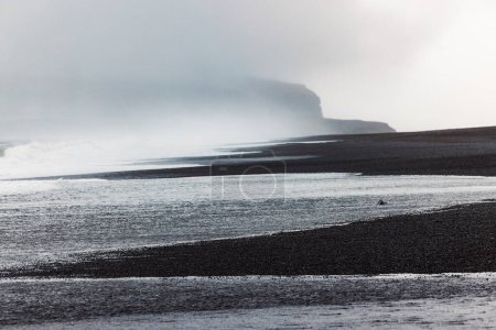 Volcanic Black Sand Beach with a view of Reynisdrangar. Waves crashing on the black sand beach. Vik, Iceland. High quality photo