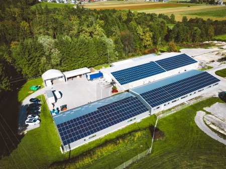 Sonnenkollektoren auf dem Dach eines großen Industriegebäudes oder einer Lagerhalle. Industriebau auf dem Land in Slowenien mit Wohnhäusern im Hintergrund. Hochwertiges Foto