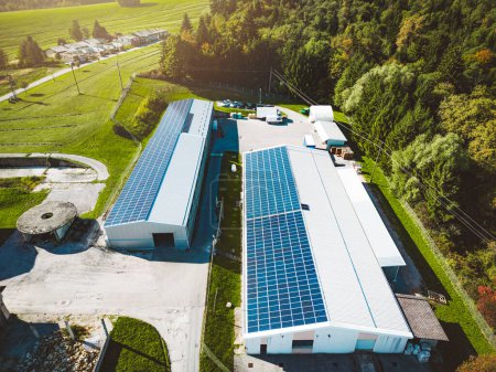 Foto de Paneles solares instalados en un techo de un gran edificio industrial o un almacén. Edificio industrial en el campo de Eslovenia con casas residenciales en el fondo. Foto de alta calidad - Imagen libre de derechos