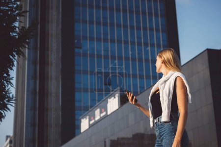 Photo for Young caucasian woman in an urban modern setting, skyscrapers in the bacground, using a mobile device. Business woman on a break. - Royalty Free Image