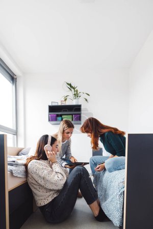 Foto de Grupo de tres compañeras de cuarto, estudiante universitaria, jóvenes caucásicas, pasando tiempo juntas en su habitación, estudiando, hablando, divirtiéndose, riendo. - Imagen libre de derechos