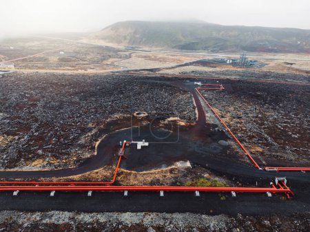Foto de Central Geotérmica, central eléctrica de agua caliente en Islandia. Vapor saliendo de las chimeneas de la planta, grandes tubos rojos corriendo por los terrenos llenos de agua caliente. Sostenible, energéticamente eficiente - Imagen libre de derechos