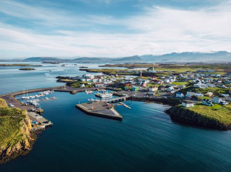 Foto de Hermosa vista aérea del puerto de Stykkisholmskirkja con barcos pesqueros en la ciudad de Stykkisholmur en el oeste de Islandia. Vista de la ciudad desde el acantilado Sugandisey con faro. Famosas casas coloridas - Imagen libre de derechos