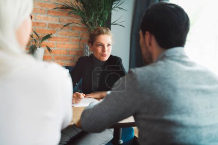 Foto de Meeting with clients. Caucasian woman, designer, meeting with her clients, sitting by the desk, consulting on a project. Business meeting. Caucasian people having a meeting in an office. - Imagen libre de derechos