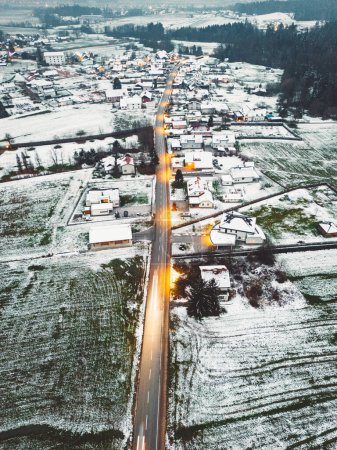 Photo for Aerial view of suburban community in winter time in the evening. Snow on the grounds, dark, street lights shining. - Royalty Free Image